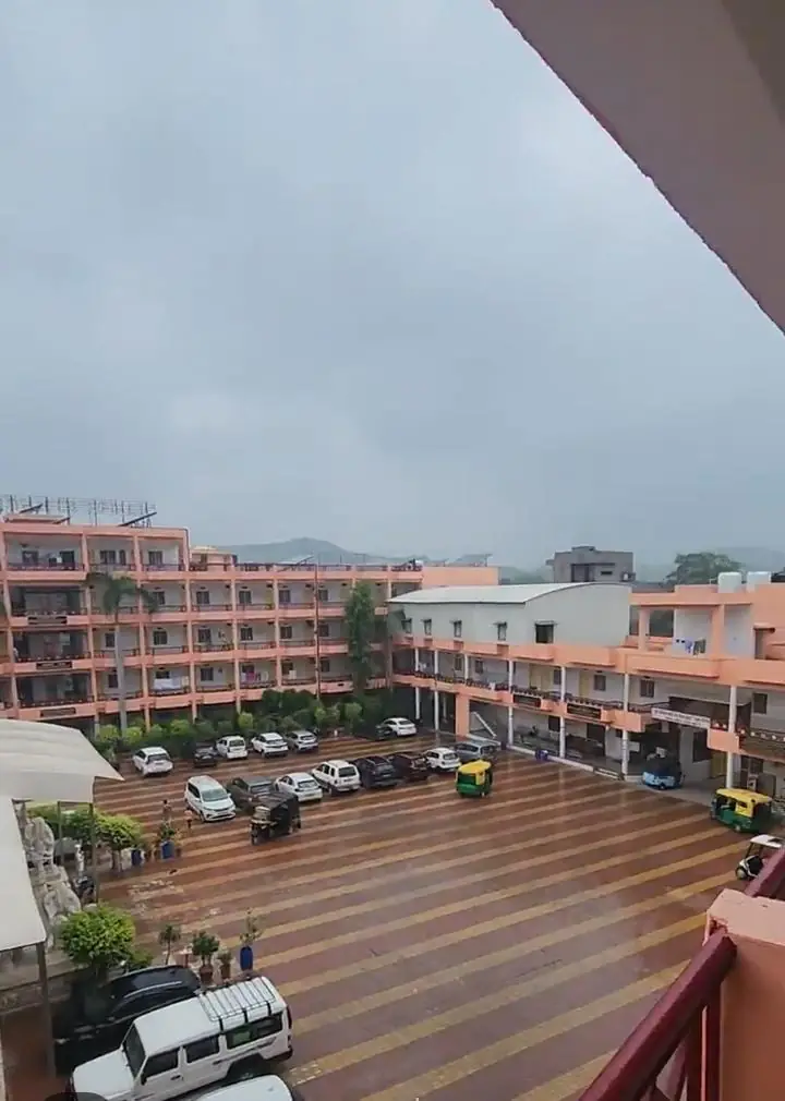 Multi-storey lodging building overlooking a large tiled courtyard with parking